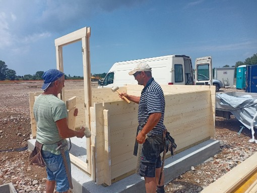 lavoro di montaggio casetta in legno di piccole dimensioni due artigiani con cappellino per proteggersi dal sole stanno montando il sembrante della porta