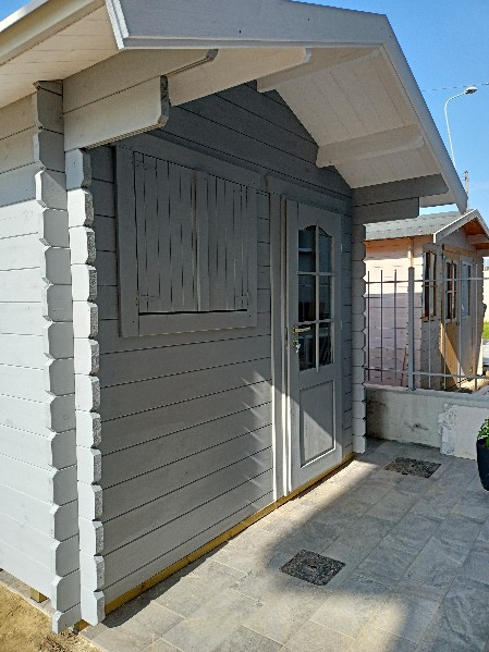 casetta in legno con ampia sporgenza tetto sul lato portya colori grigio e bianco, porta con vetro e finestra con scuri